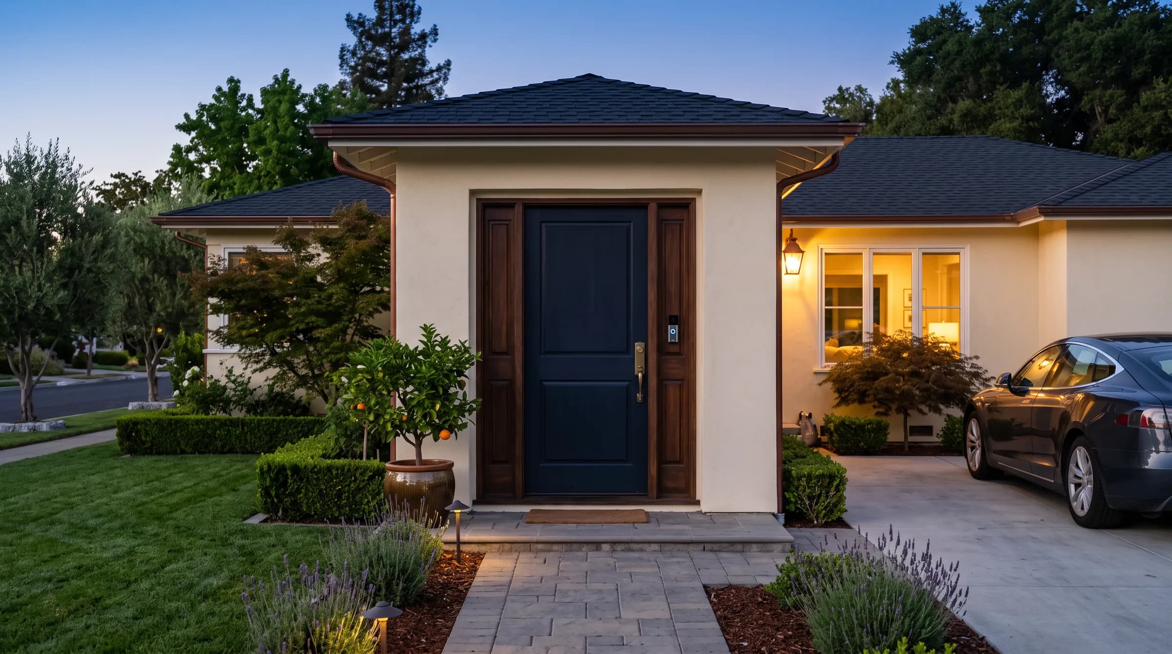 A Cupertino front door at dusk: a dark painted door in its original 1950s opening, a brass handleset at hand height, a small video doorbell on the casing beside it, and the front room lit behind the window.